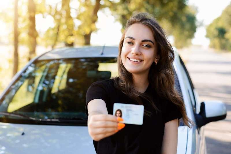 A girl with a driver's license in front of a car