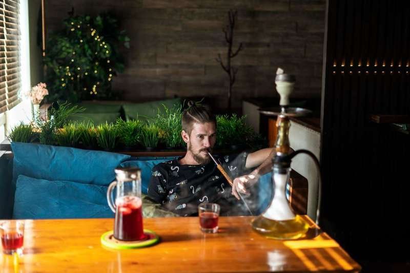 A man smokes a hookah while sitting on a sofa