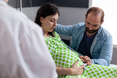 A husband holds his pregnant wife's hand in a hospital
