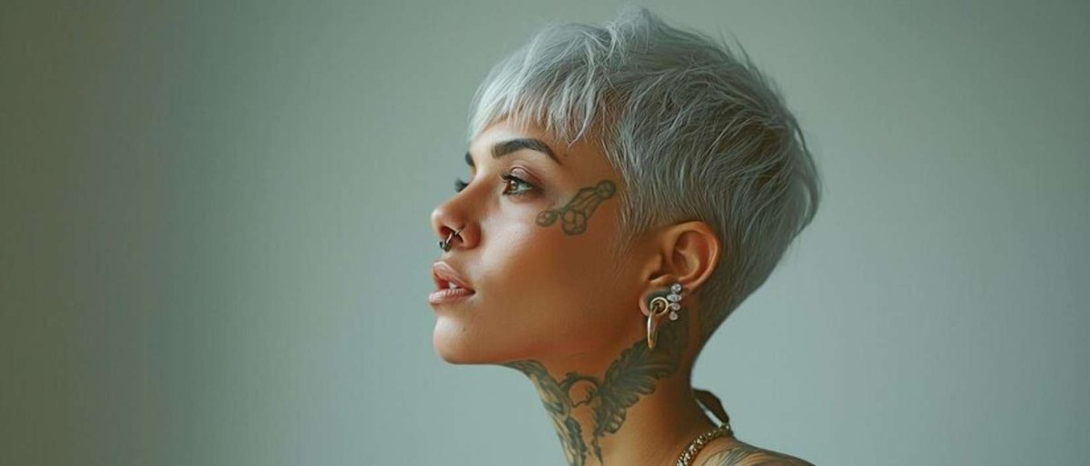 A portrait of a woman with short silver hair and intricate facial tattoos