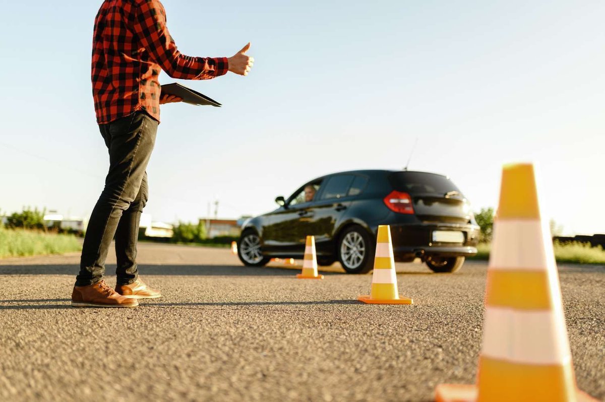 An instructor helps a student navigate between cones during a driving lesson.
