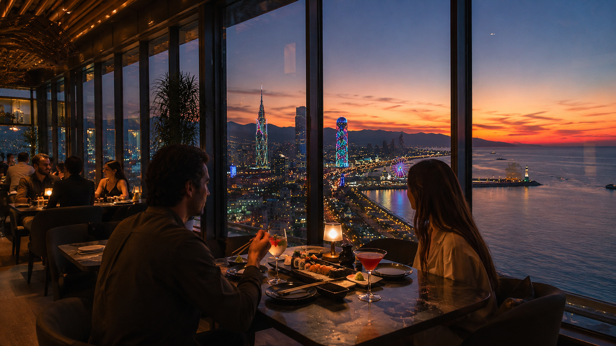 Guests dine near panoramic windows with sushi, cocktails and the Batumi coastline visible beyond the glass.