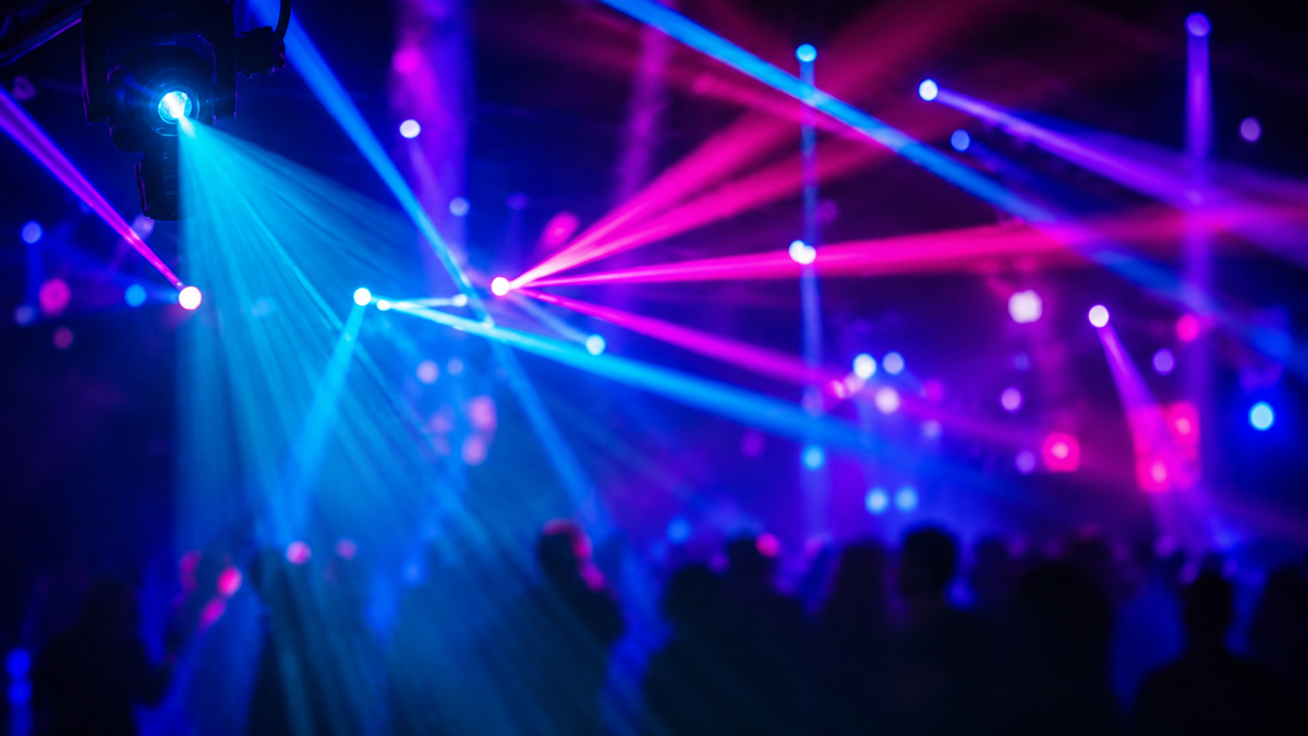 Colourful stage lights over a dance floor with silhouettes of people dancing.
