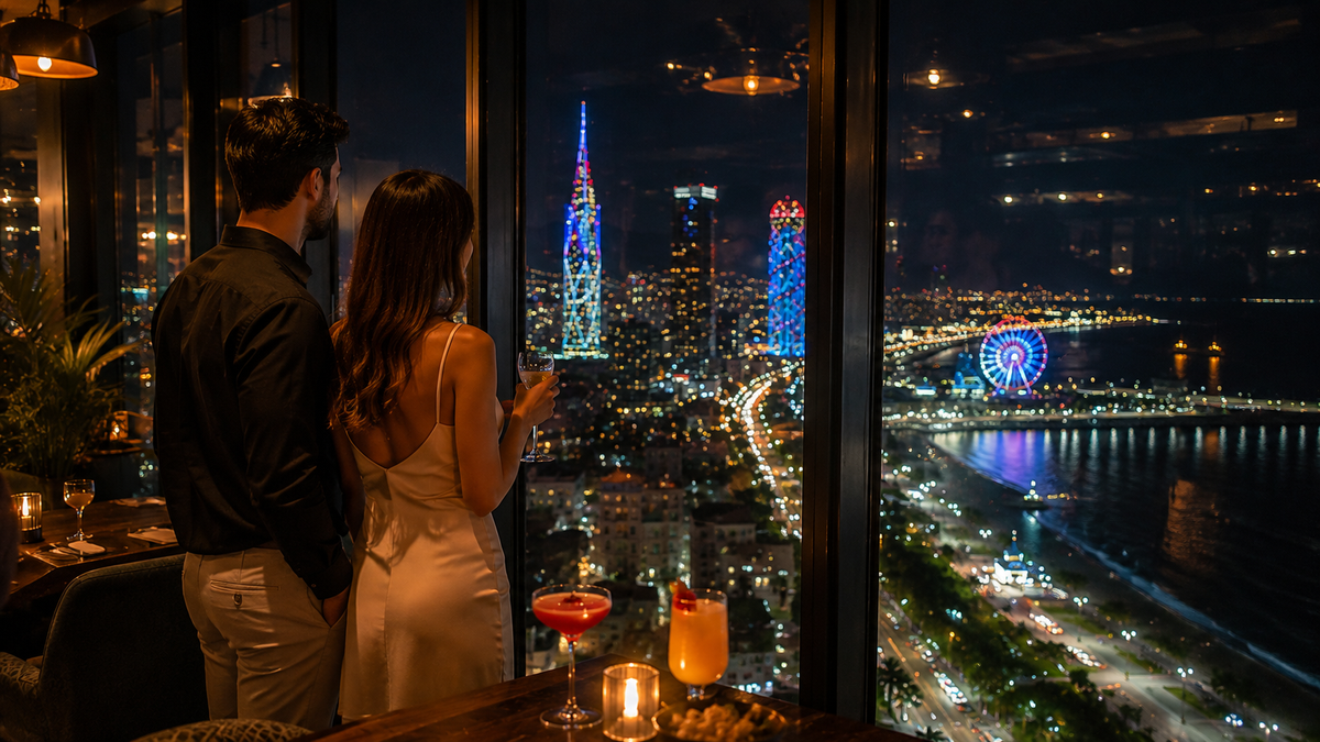 Two guests look out from a rooftop restaurant as Batumi’s night lights reflect across the windows.