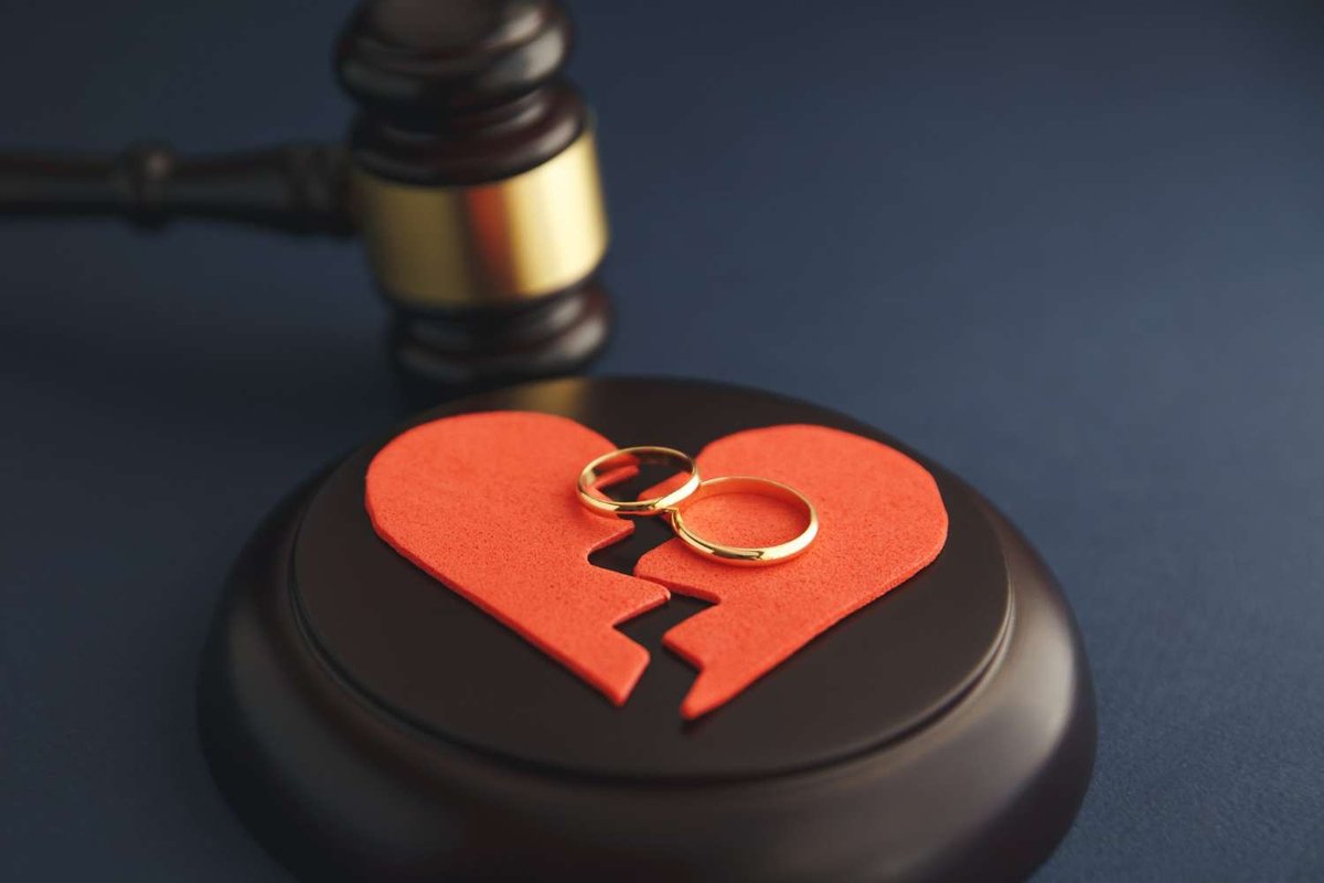 A judge’s gavel hovers above a split red heart cutout with two gold wedding rings, symbolizing a divorce case in the Georgian court system.