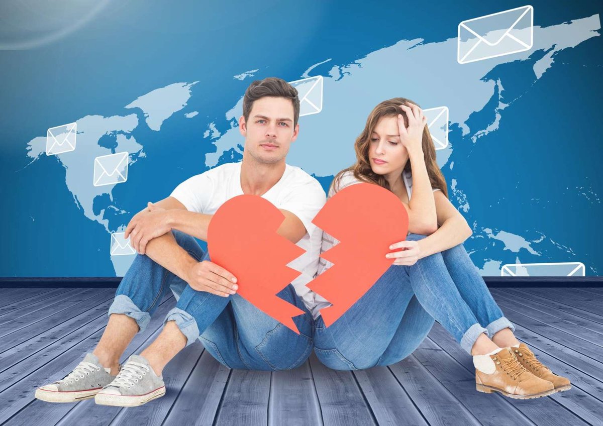 A man and woman sit apart holding two halves of a torn red paper heart, with a world map and email icons symbolizing a long-distance divorce in the background.