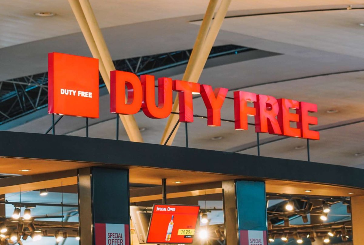 A large illuminated red “Duty Free” sign hanging from the ceiling above a terminal shop entrance, with a special offer price display visible below.