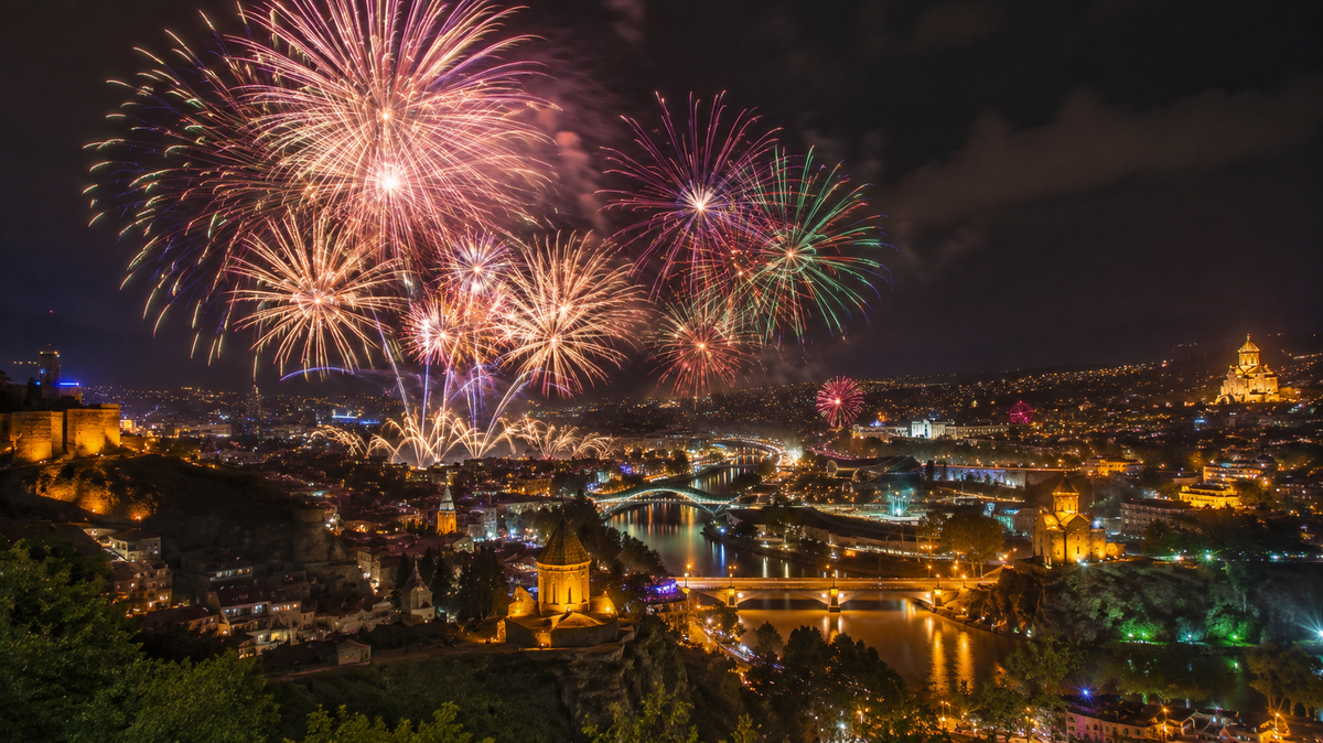 A grand fireworks display bursts above the Mtkvari river and Tbilisi's illuminated skyline, closing the Independence Day celebrations.