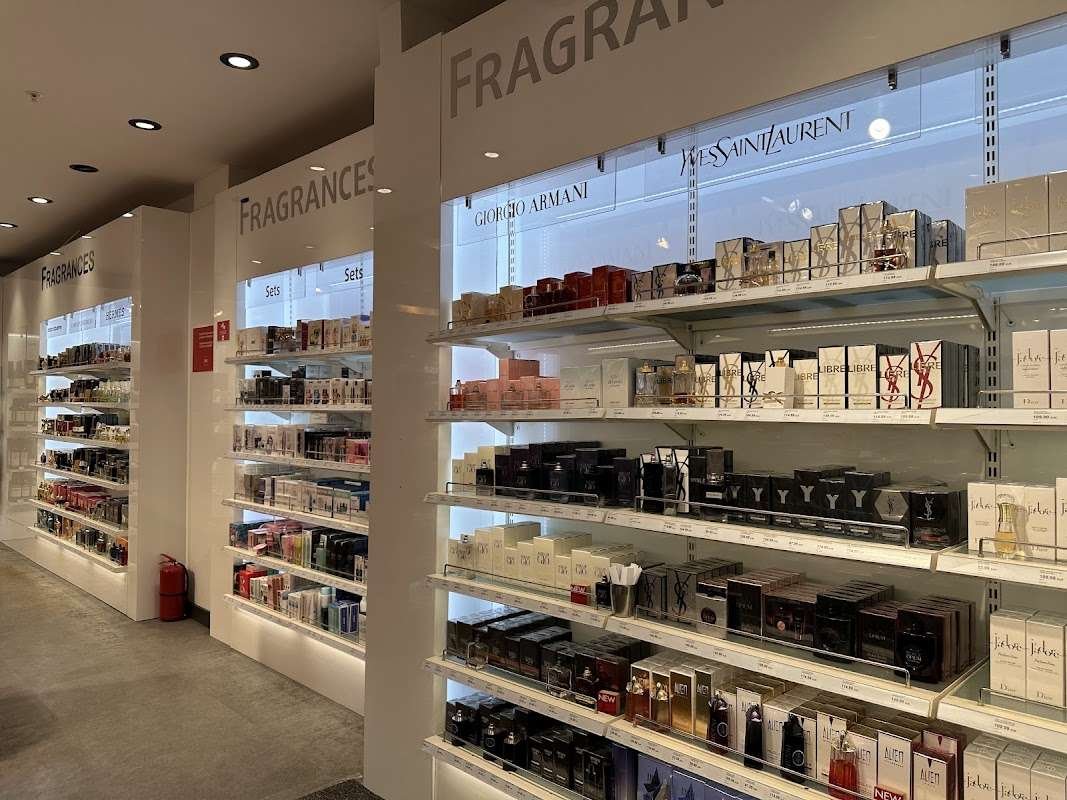 Rows of perfume boxes from Giorgio Armani, Yves Saint Laurent, and Dior displayed on lit shelves in an airport duty free fragrance aisle.