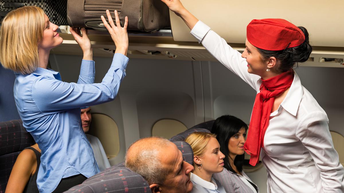Приветливая стюардесса помогает пассажиру разместить багаж в  багажное отделение