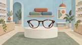 Иллюстрация салона оптики: очки в коричневой оправе на подиуме, футляры и оправы на полках.