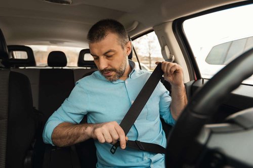 A man buckles his seatbelt behind the wheel, illustrating Georgia's mandatory seatbelt rule for front-seat passengers.