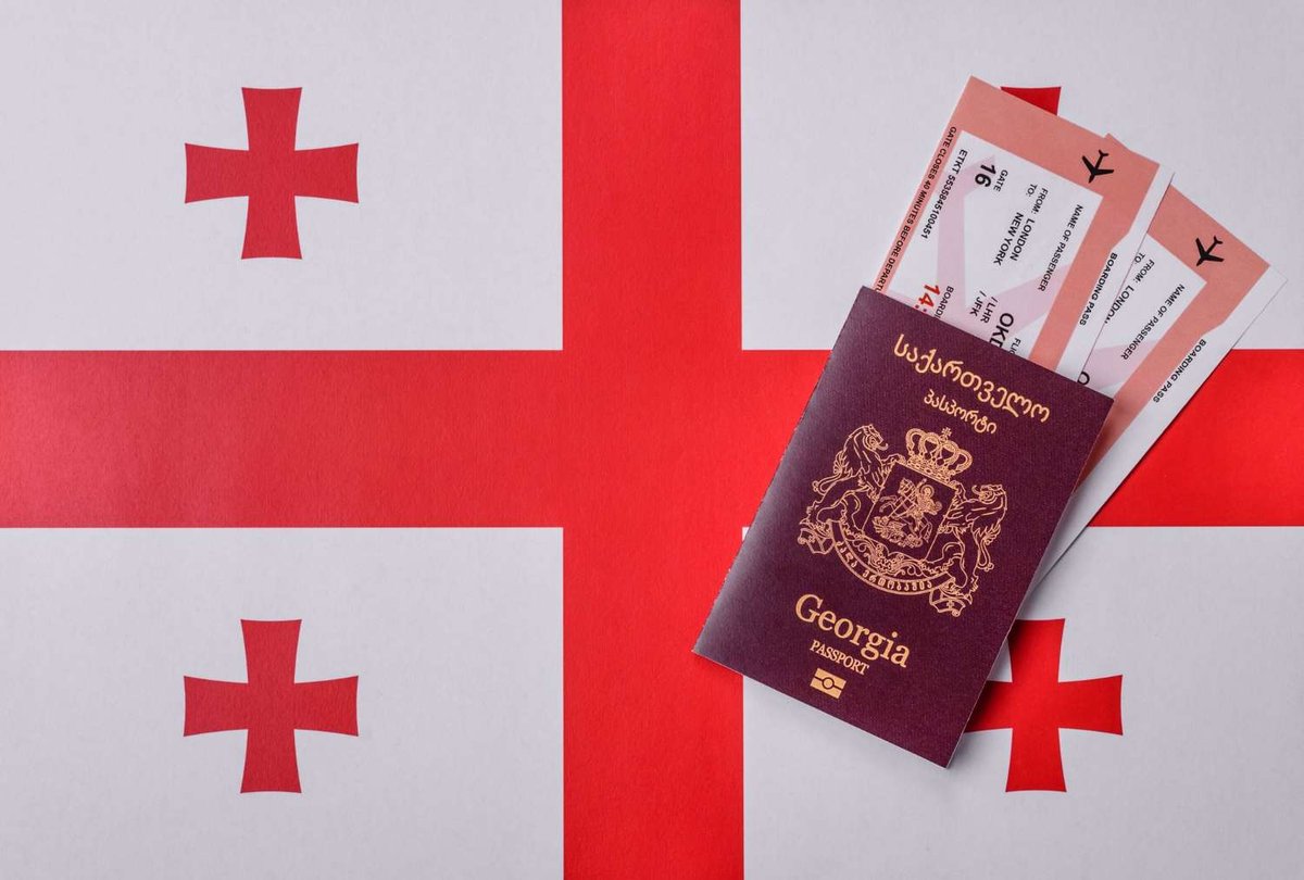 A maroon Georgian passport and two London–New York boarding passes resting on the white and red cross flag of Georgia.