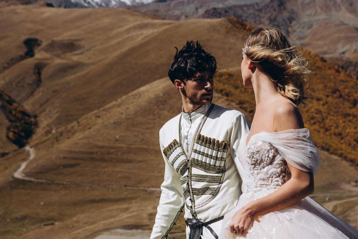 Happy couple groom in traditional costume and bride on top of a mountain with sands in the background