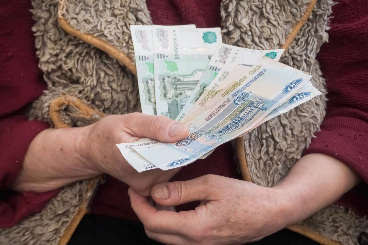 Weathered hands fan out a stack of Russian ruble banknotes against a wool vest and red sweater.