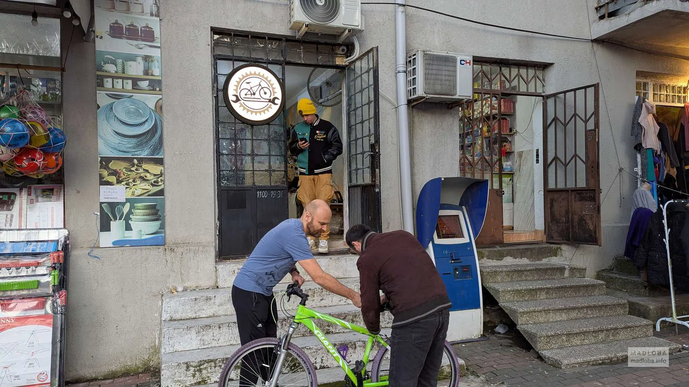 Два мастера чинят велосипед перед магазином J-Bike