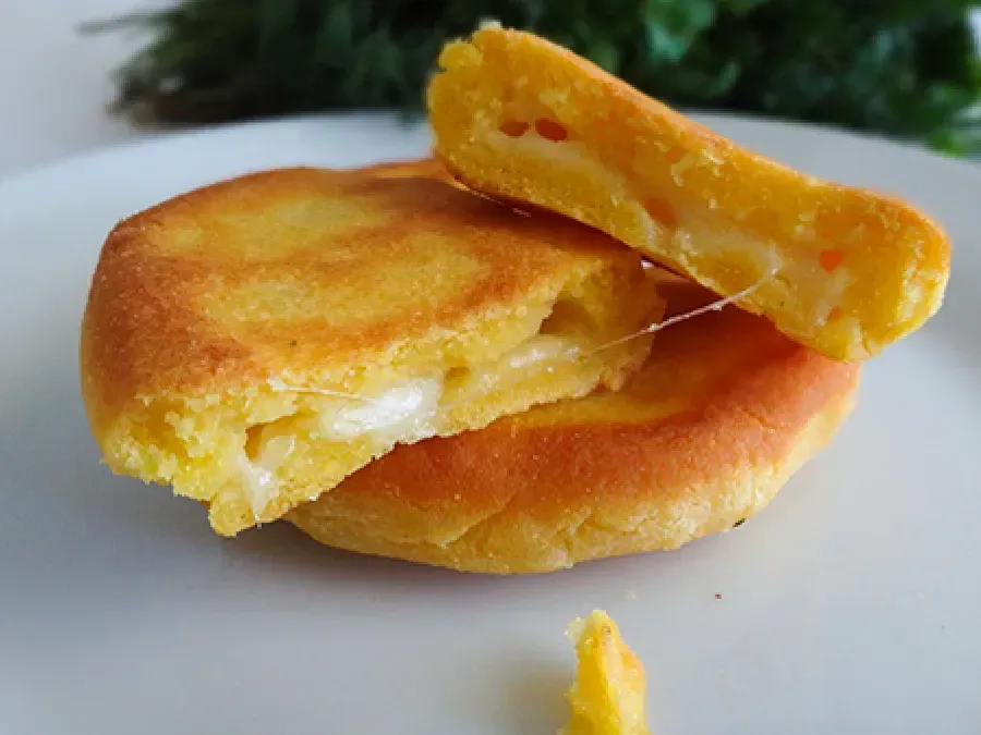 A torn piece of golden cornbread reveals a stretchy melted cheese center, served on a white plate.