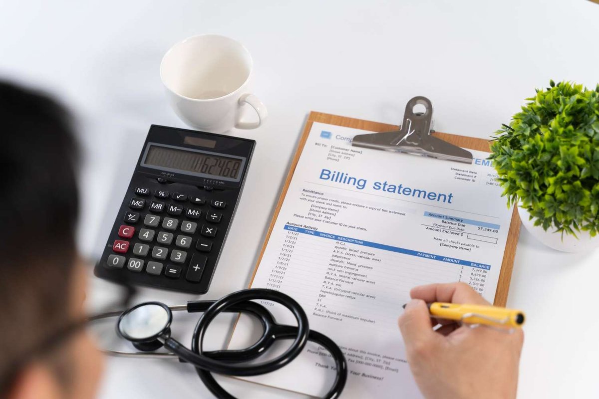 A person calculates figures beside a medical billing statement and stethoscope, illustrating the paperwork behind claiming reimbursement.