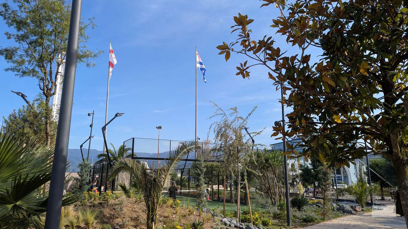 Вид на корты и развевающиеся флаги Грузии и Аджарии на фоне гор создаёт динамичный, вдохновляющий пейзаж.