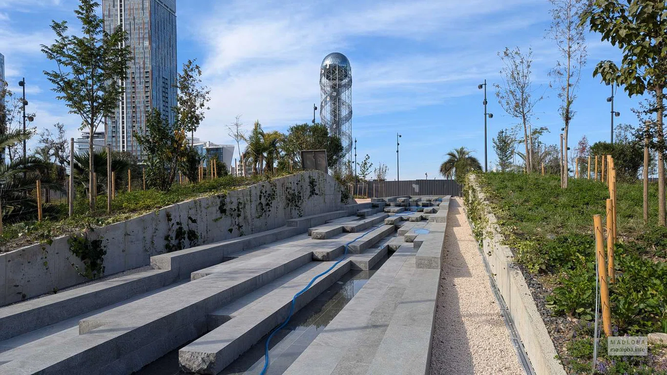 Современная архитектура сочетается с природным рельефом — лестничный водный каскад ведёт взгляд к Алфавитной башне и небоскрёбам Батуми.