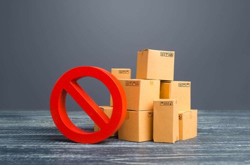 A large red prohibition sign stands next to a pile of sealed cardboard boxes marked with fragile and recycling symbols.