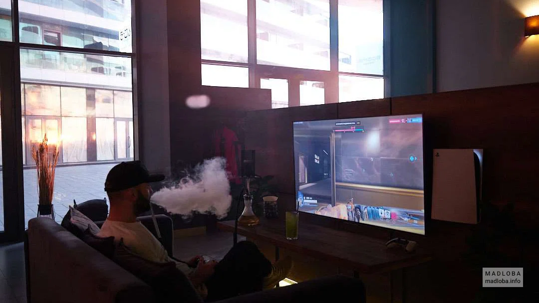парень курит кальян и играет в приставку в "Nuahule Smoke" в Батуми