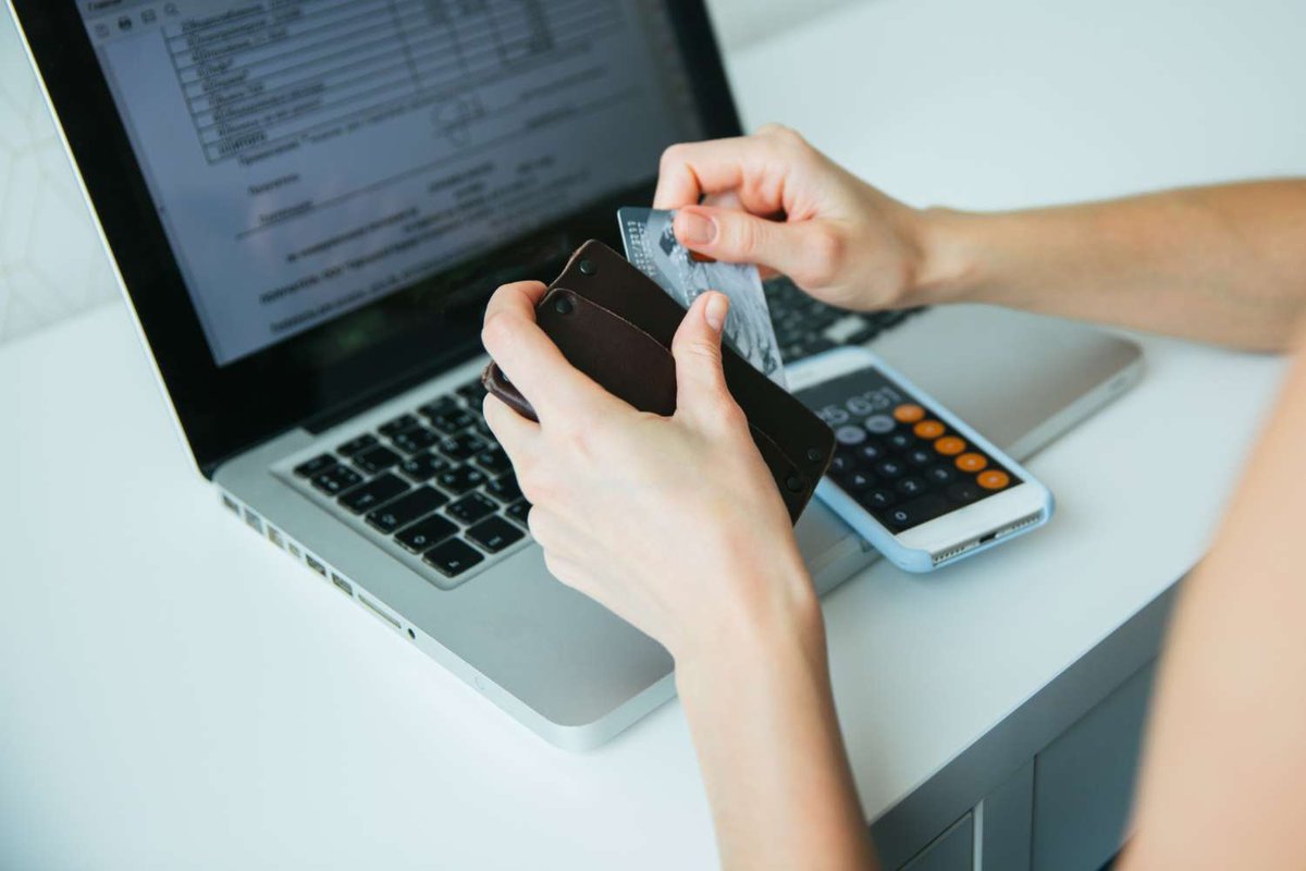 Hands holding a credit card and wallet beside a calculator and laptop showing a spreadsheet — illustrating the cost of IT courses and programming classes in Tbilisi, Georgia.