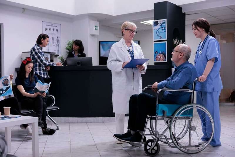 A wheelchair-bound pensioner talks to a senior doctor about an appointment while being assisted by a trained nurse at a private clinic.