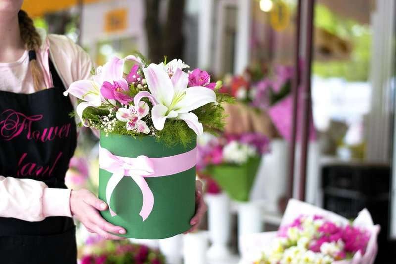 Hands of a woman holding a green flowerpot with lilies and eustoma.