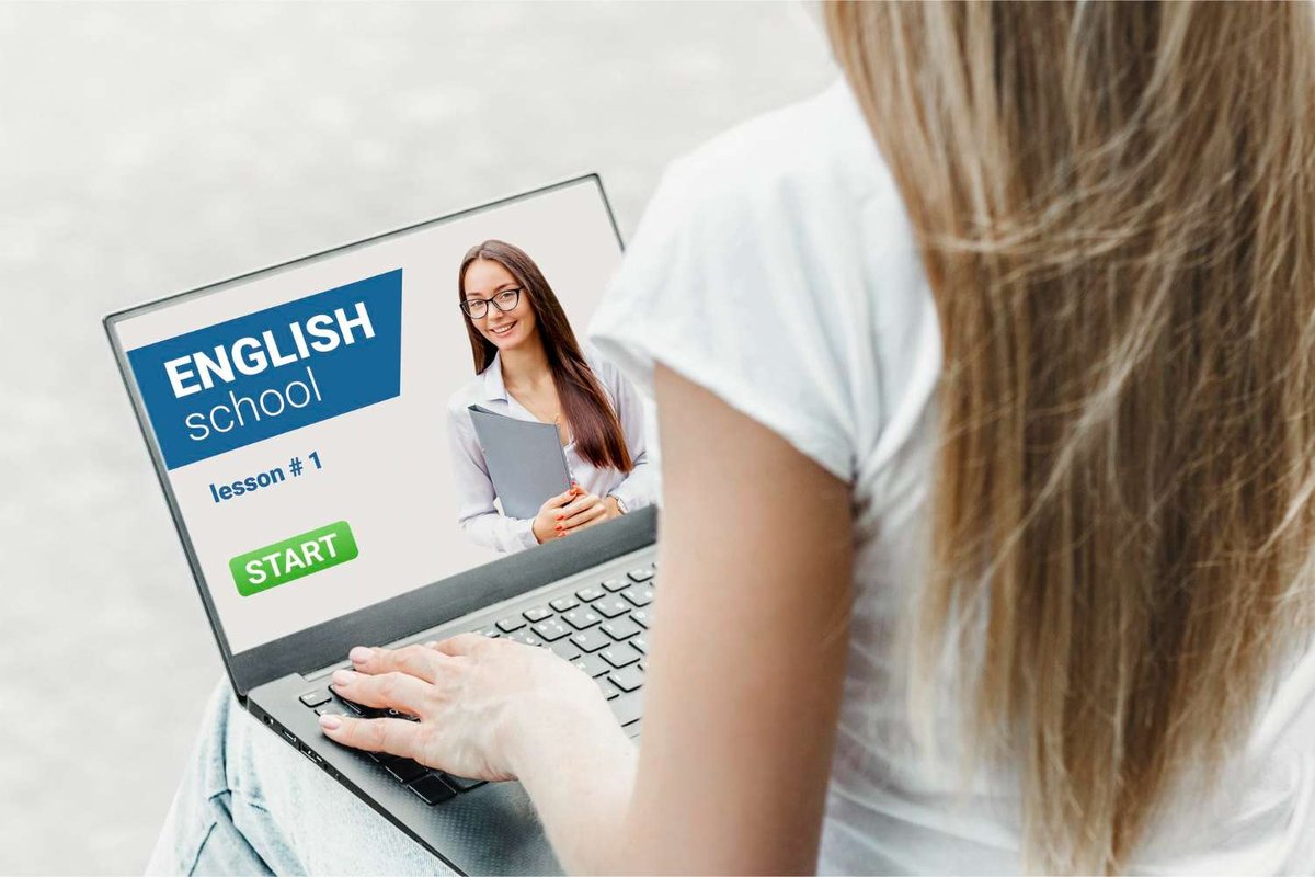 A woman sits at her laptop displaying a video call with an English teacher holding a folder, on a screen labeled “English School, lesson 1.”