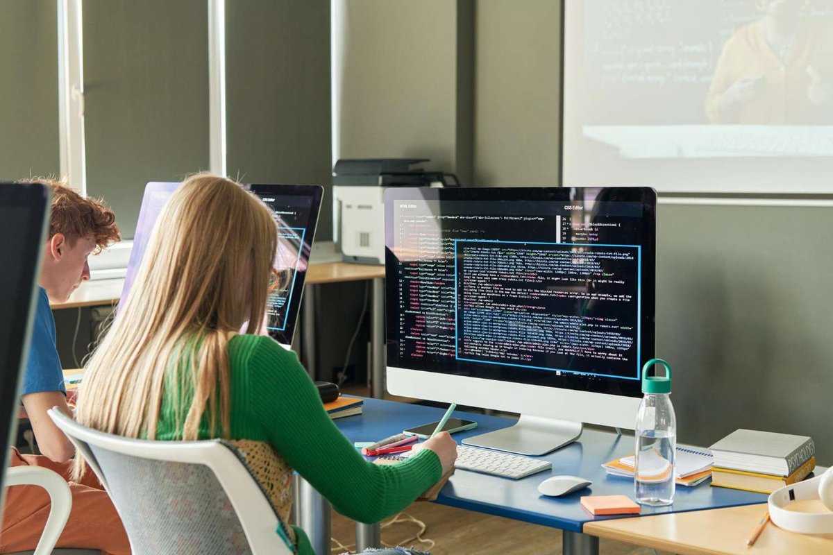 Students coding at desktop monitors with HTML and CSS editors open in a classroom — illustrating free IT programs and coding courses in Tbilisi, Georgia.