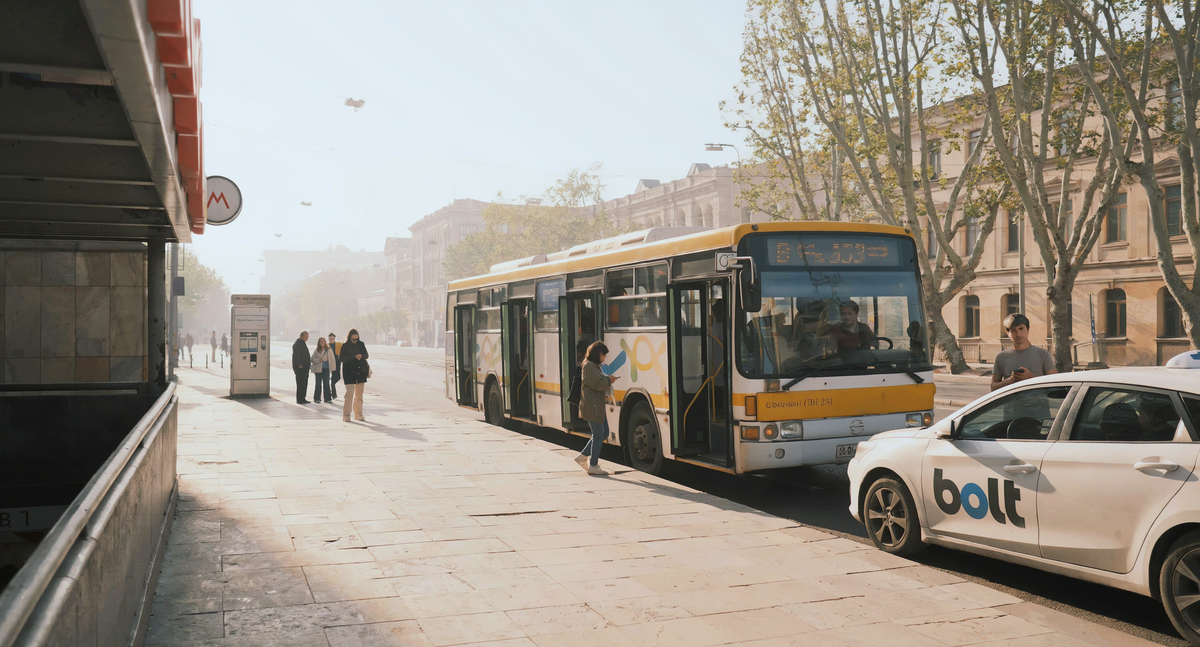 Passengers board a city bus at a metro stop while a Bolt taxi waits at the curb, showing the cheap daily transport options in Tbilisi.