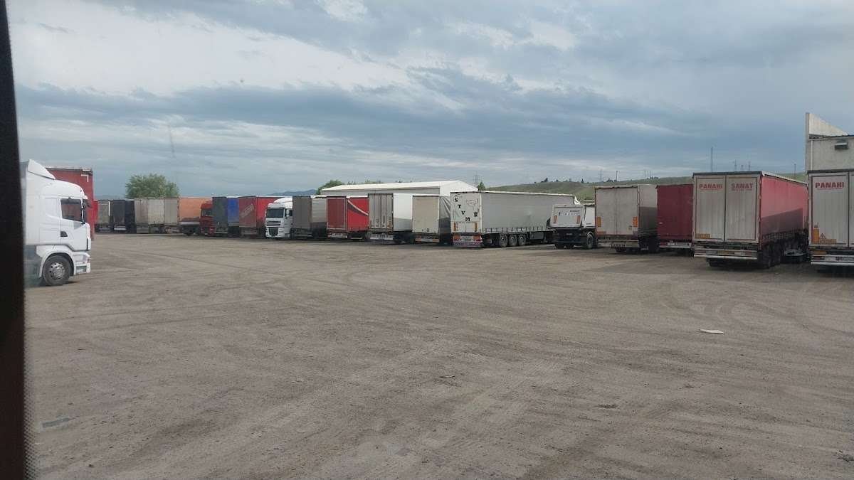 An officer monitoring the electronic queue system beside a line of freight trucks waiting at a barrier gate, with mountains in the distance.