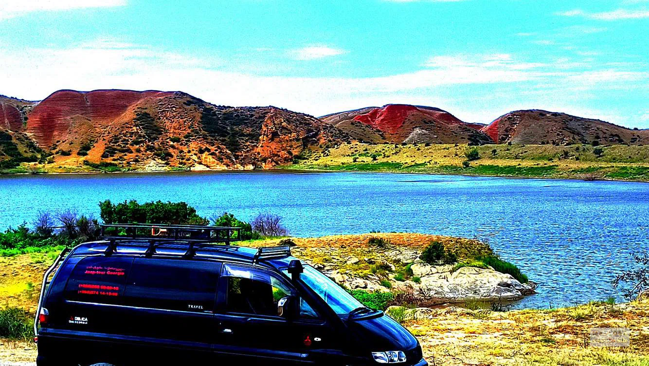 Яркое сочное Водохранилище Мравальцкаро на фоне цветных гор и с машиной на переднем плане