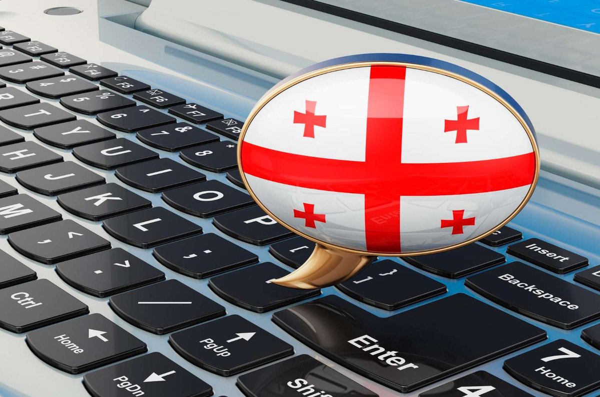 A speech bubble with the Georgian flag rests on a keyboard, illustrating the language barrier machine translation struggles to bridge.