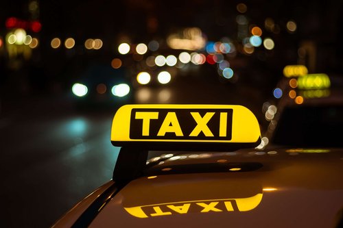 Yellow and black taxi sign on the roof of a car at night