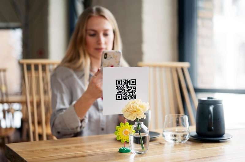 A woman scans a medium-sized QR code at a restaurant to leave a review