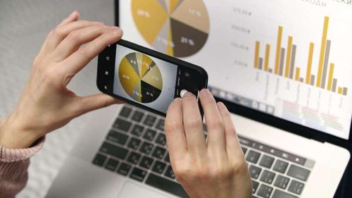 A woman's hand takes a mobile photo of statistical data on a laptop screen