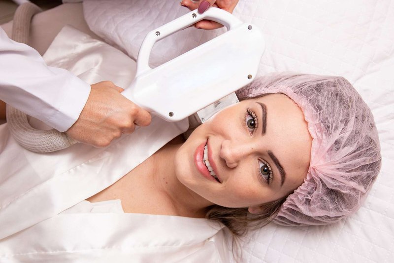 A smiling girl during a cosmetology procedure using special equipment.