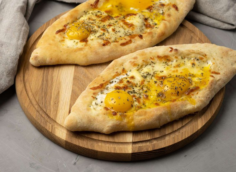 baked-adjarian-khachapuri-with-whole-egg-yolk-wooden-board-traditional-dish-top-view.jpg