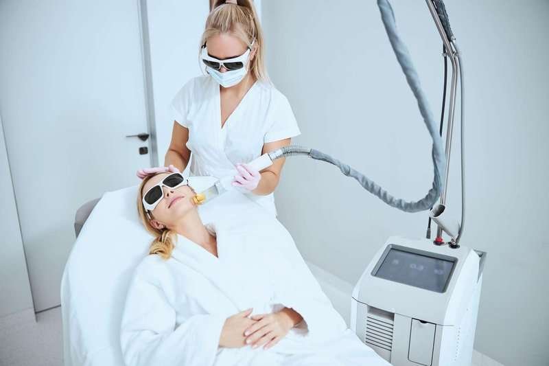 A female cosmetologist performs laser skin resurfacing using modern equipment.