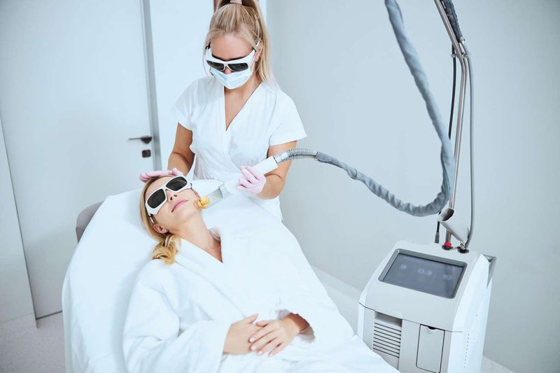 A female cosmetologist performs laser skin resurfacing using modern equipment