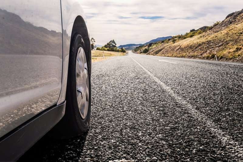 Part of a car on a road with a view of the mountains