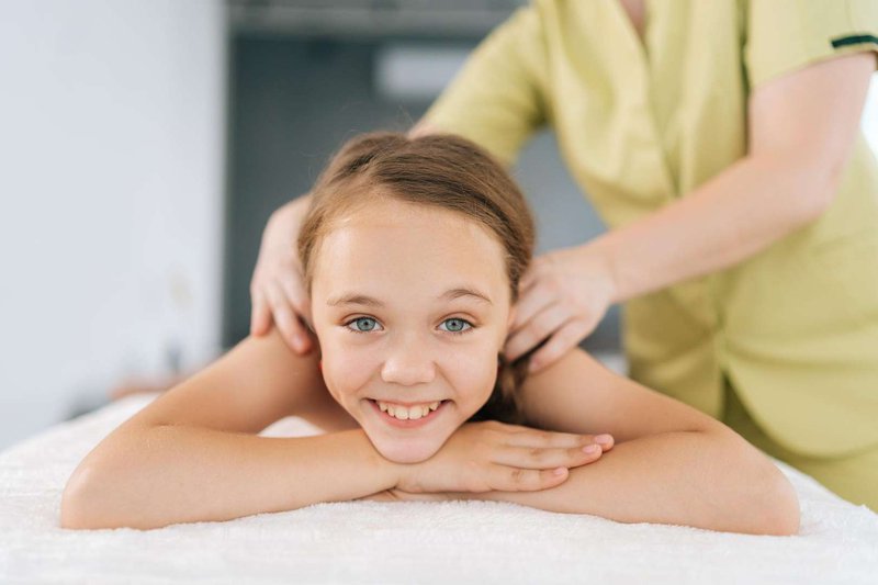 Маленькая улыбающаяся девочка на сеансе массажа