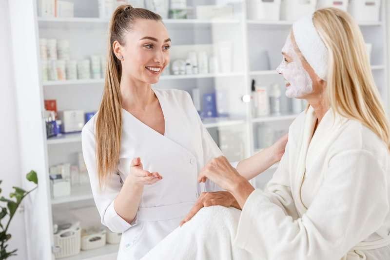 A female cosmetologist answers her client's question. Both are smiling.