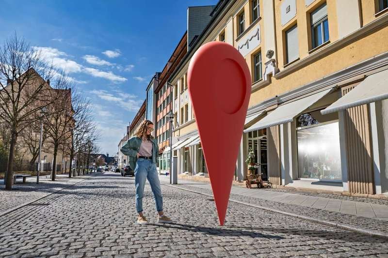 A girl stands near a building with a smartphone in her hands and a large geolocation icon next to it
