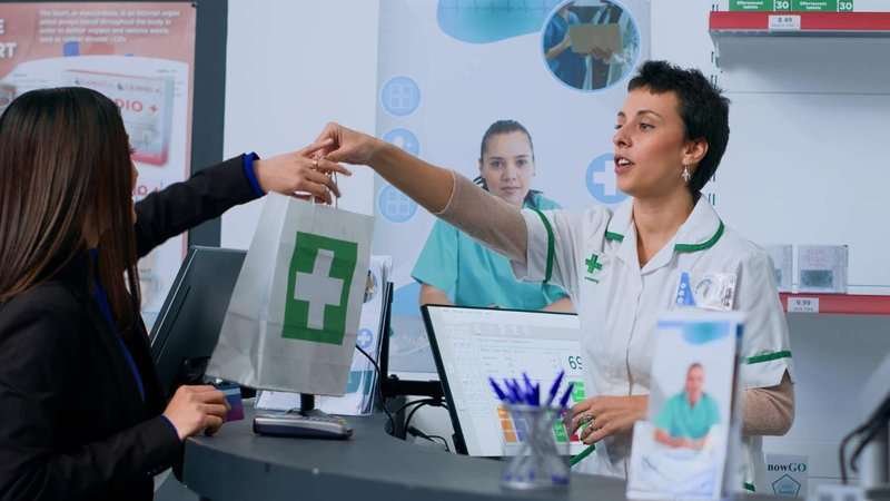 A pharmacist hands a package of medicine to a customer at a pharmacy