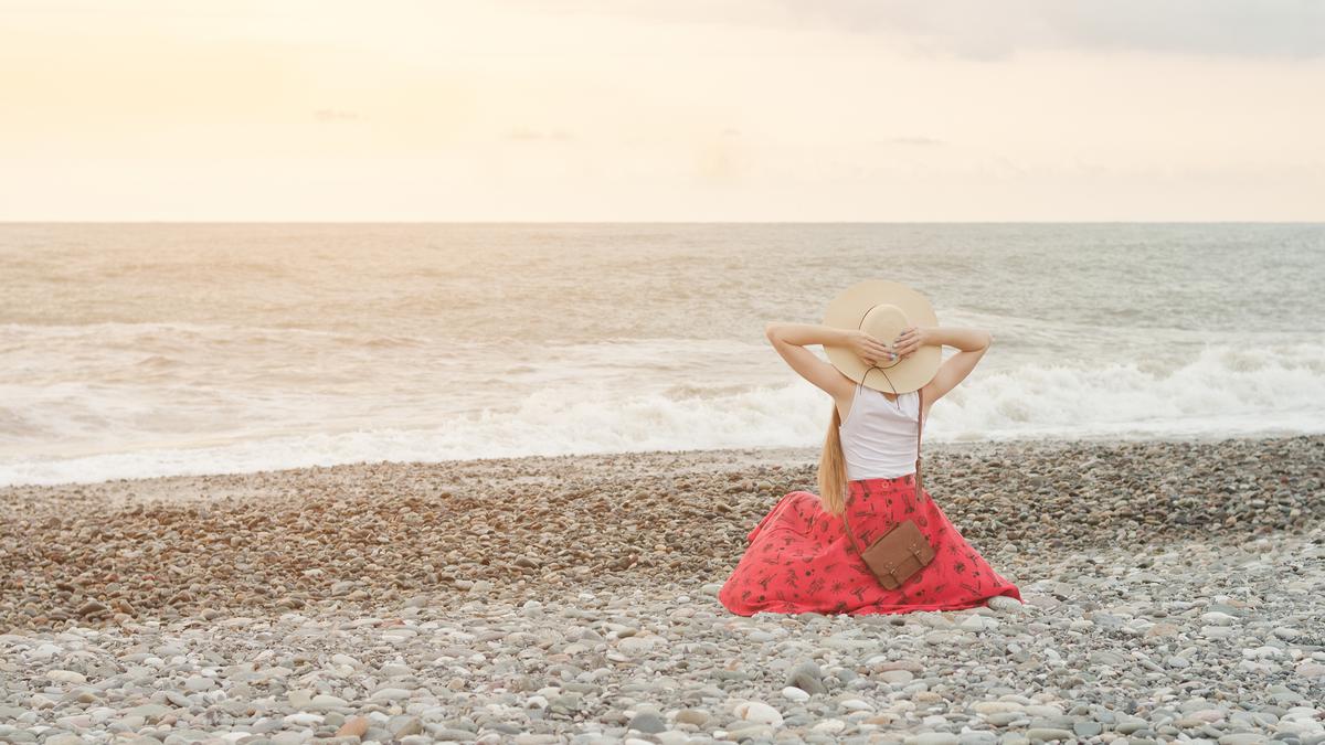 Девушка в красной юбке сидит на берегу моря в Грузии