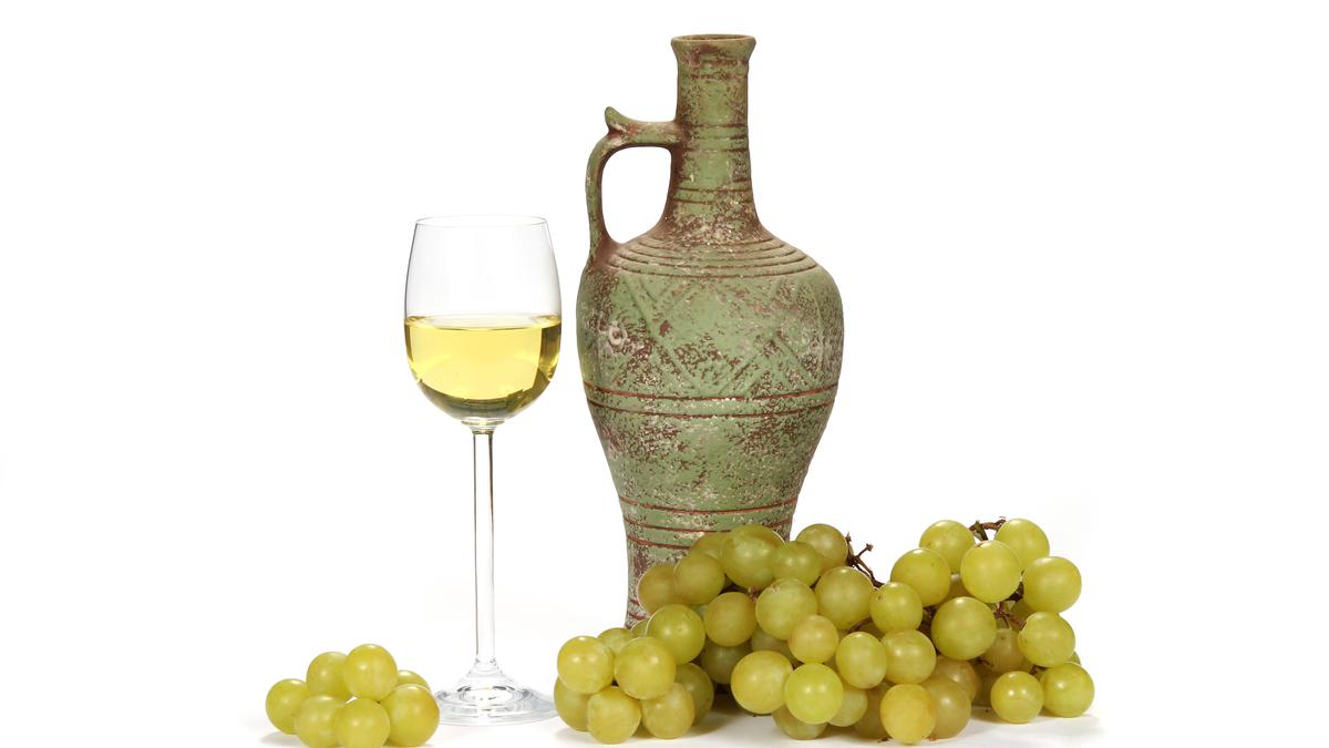 Бокал белого вина рядом с кувшином и зеленым виноградом