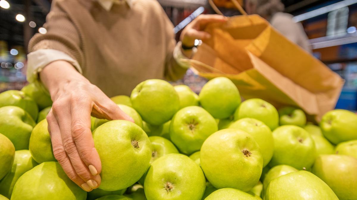 Рука пожилой женщины с бумажным пакетом берет свежее яблоко